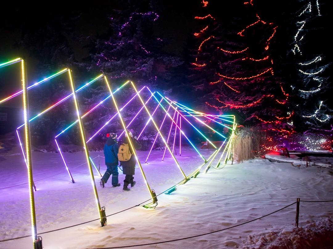 Two people walking through a tunnel of rainbow-colored neon lights in snow