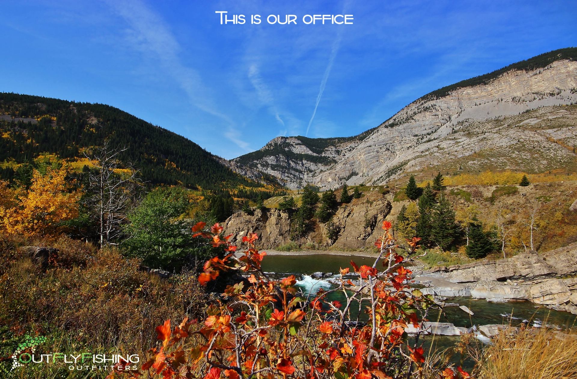 Mountain river scene with fall colors, cliffs, and blue sky.