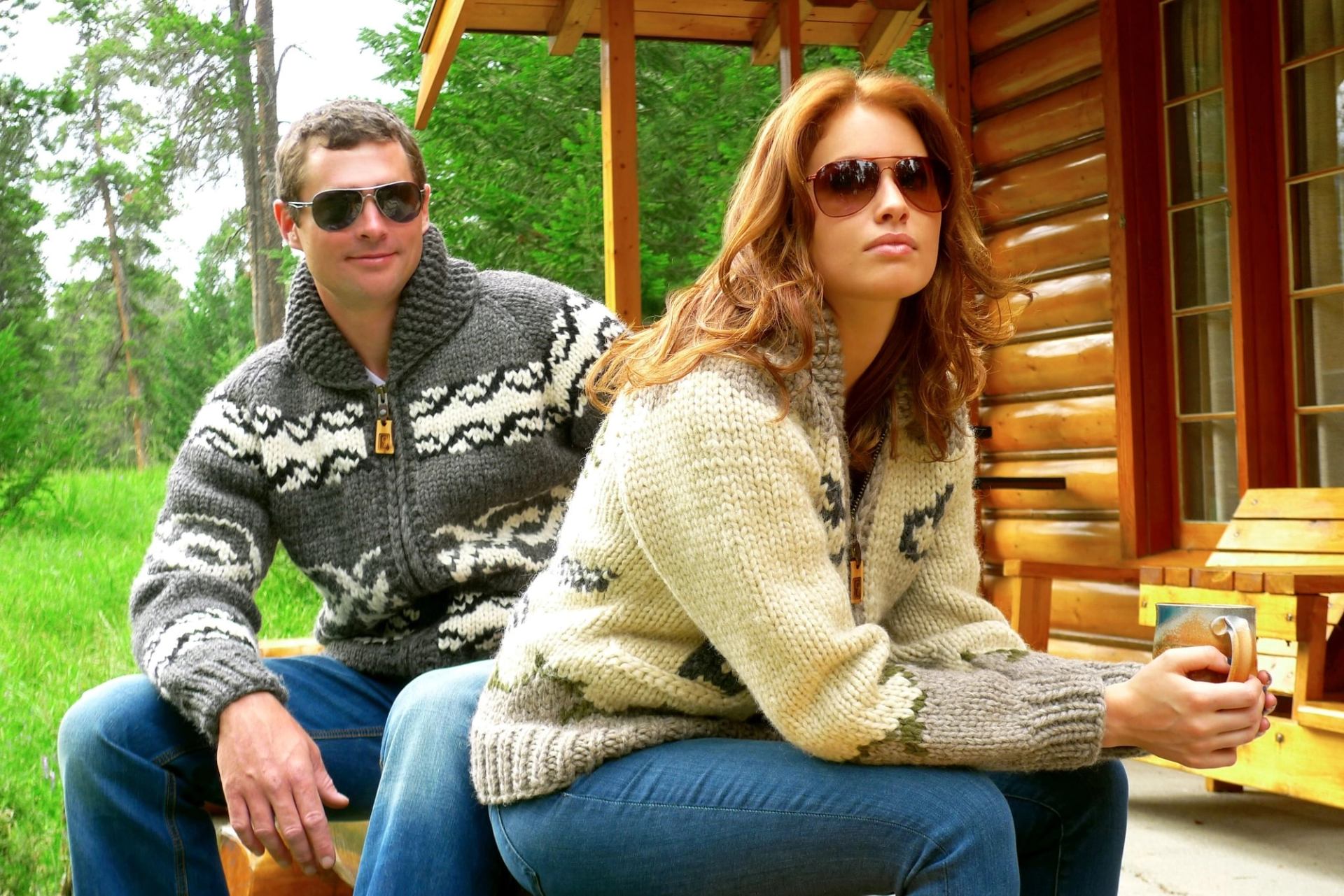People in knit sweaters and sunglasses sit on log cabin porch; one holds a mug.