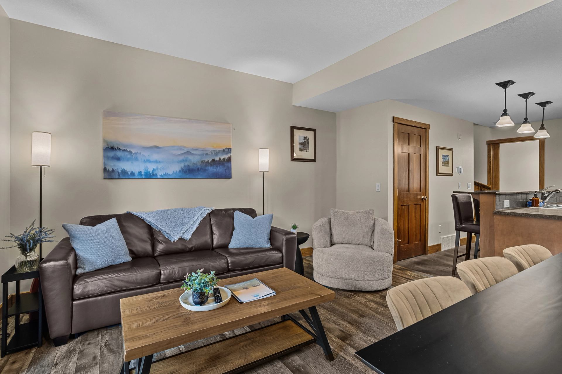 Living room with leather sofa, armchair, coffee table and adjoining kitchen.