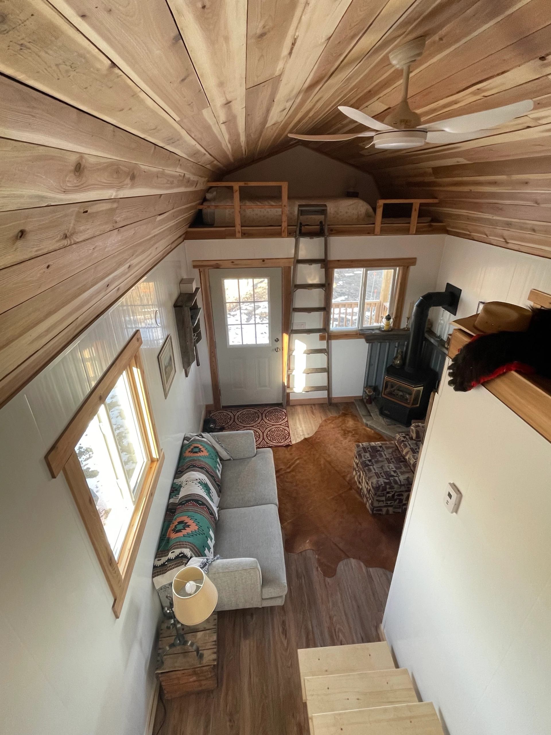 Cabin interior with wood ceiling, sofa, and loft bed accessed by ladder above the main space.