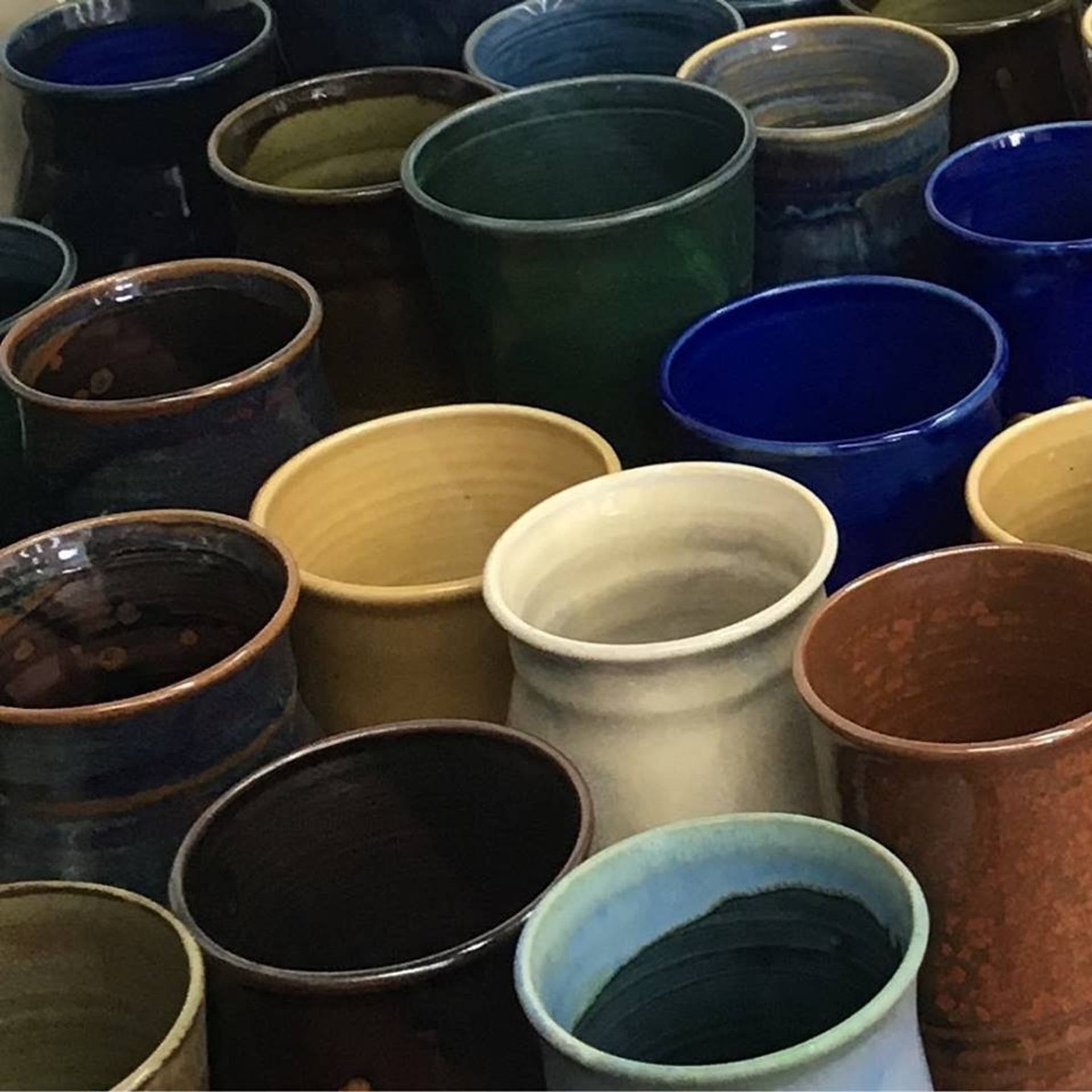 Assorted handmade ceramic cups in various colours and glazes arranged closely together.