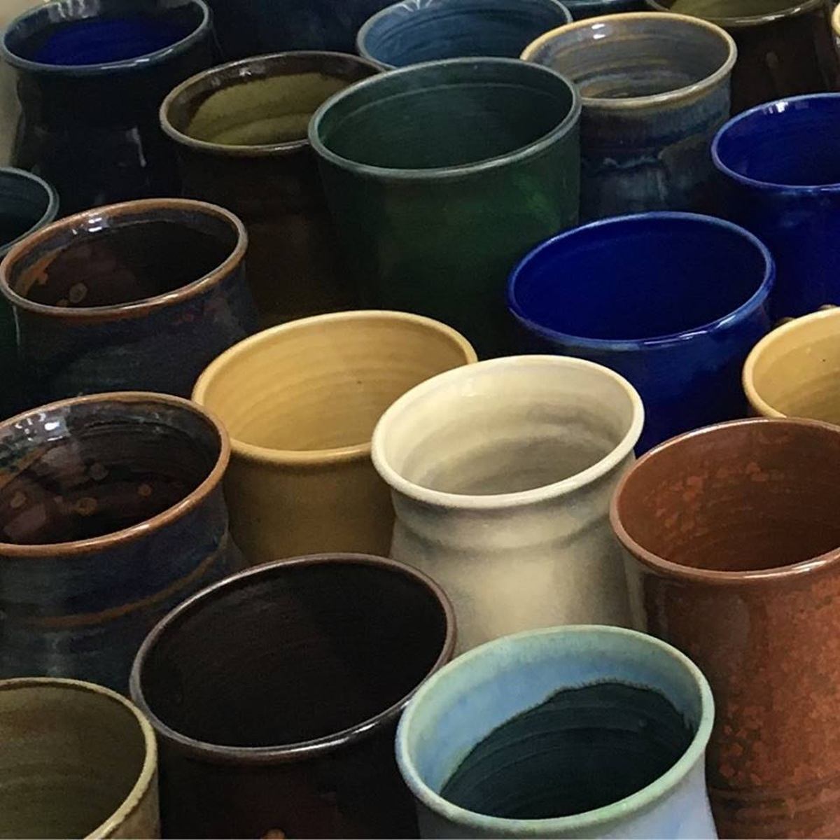 Assorted handmade ceramic cups in various colours and glazes arranged closely together.
