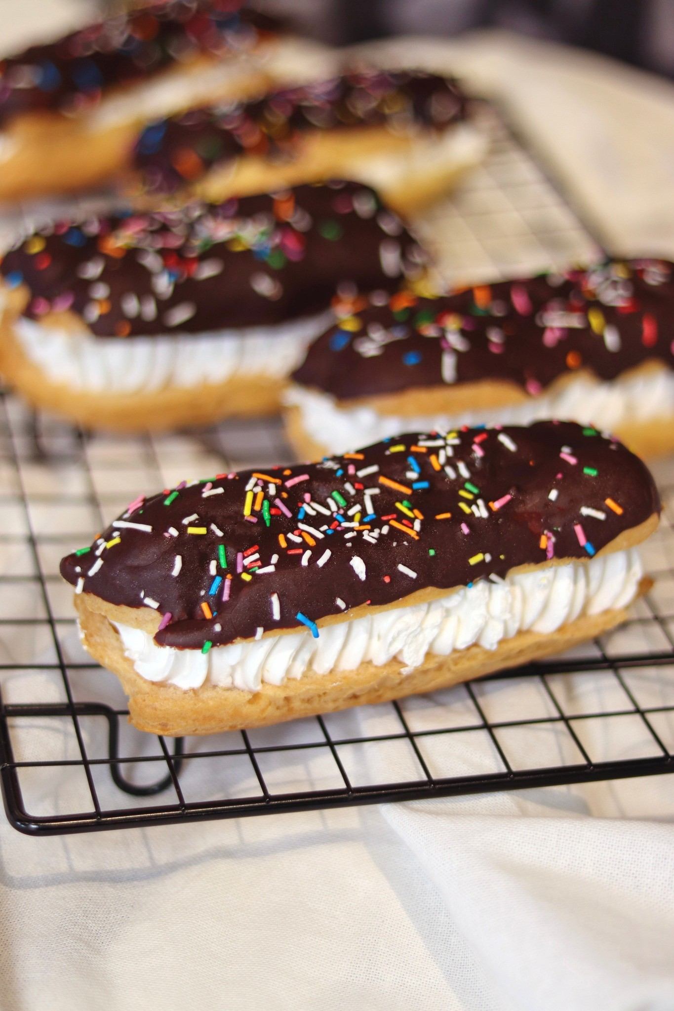 Chocolate eclair with whipped cream and sprinkles on cooling rack
