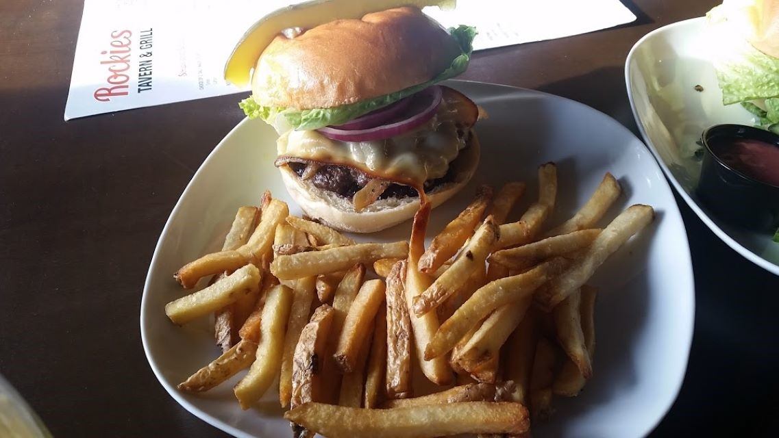Burger with fries on white plate beside Rockies Tavern & Grill menu.