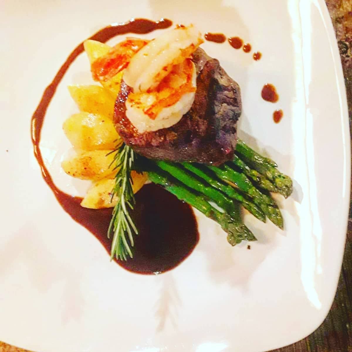 Steak topped with shrimp, asparagus, and potatoes in a gourmet plating.