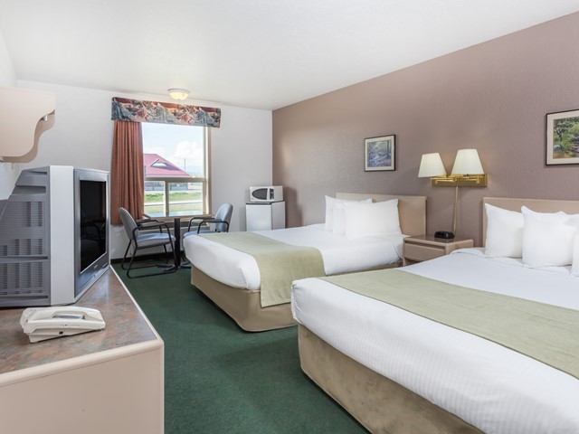 Hotel room with two queen beds, green carpet, desk, TV, and window with outdoor view.