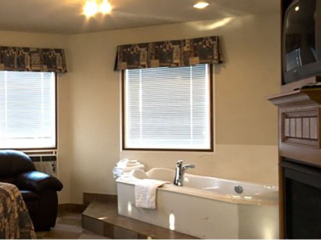 Motel room with a corner jetted tub, armchair, and windows with patterned valances.