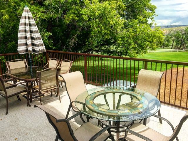 Sunny patio with glass tables, umbrella, and chairs overlooking lush green lawn and fenced pasture.