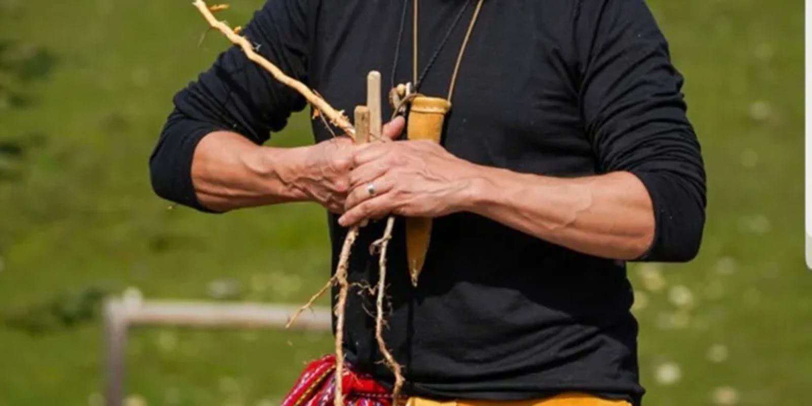 Person in black shirt holding wooden sticks and roots against blurred green background.
