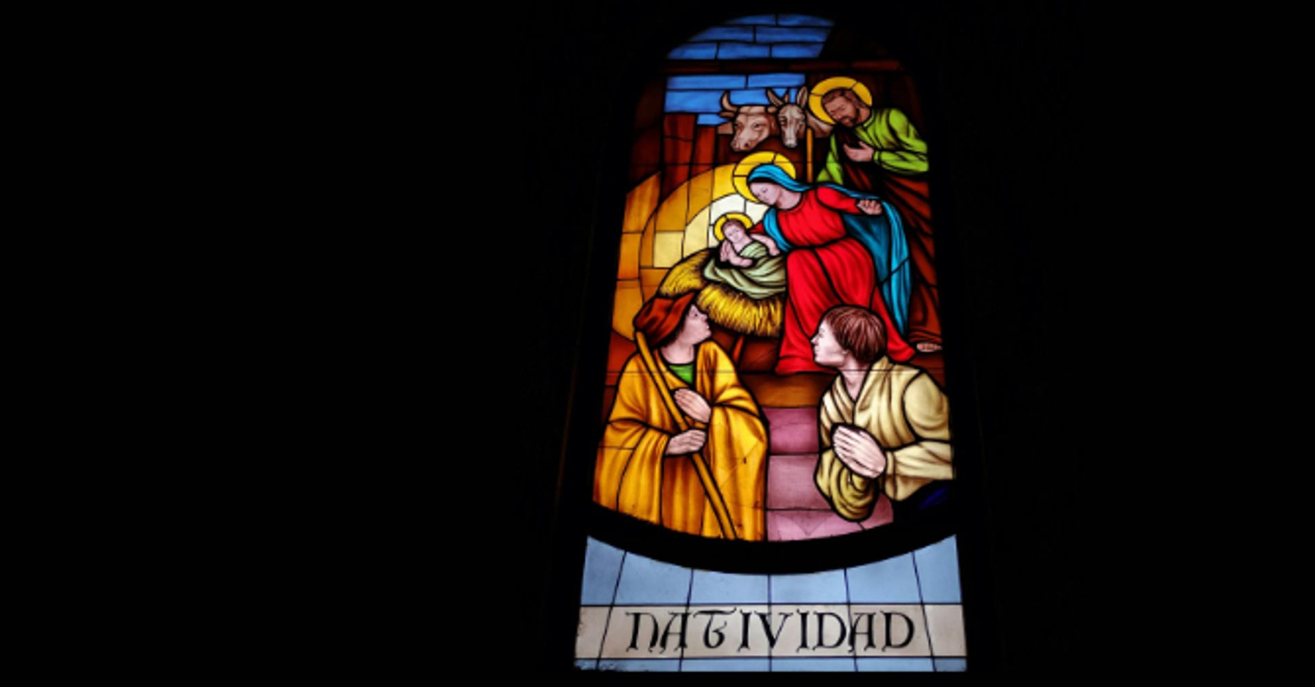 A stained-glass window shows a Nativity scene with figures gathered around an infant in a manger.