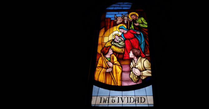 A stained-glass window shows a Nativity scene with figures gathered around an infant in a manger.