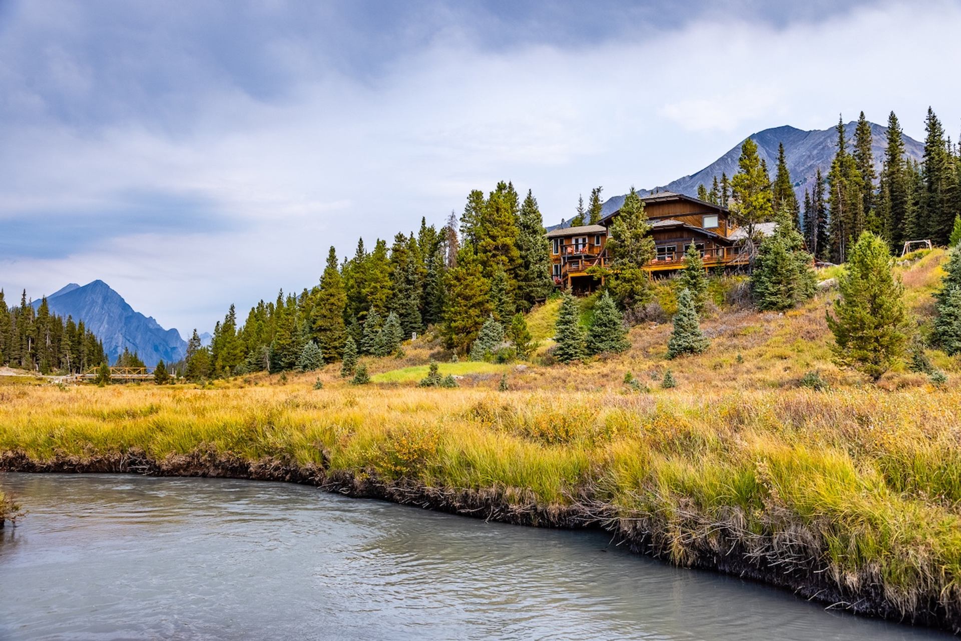 Lodge on a hillside surrounded by trees, mountains, and a winding creek.