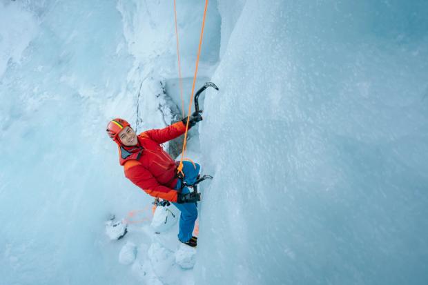 An ice climber clamped and tethered onto the ice wall stops for a smile while ice climbing in Nordegg