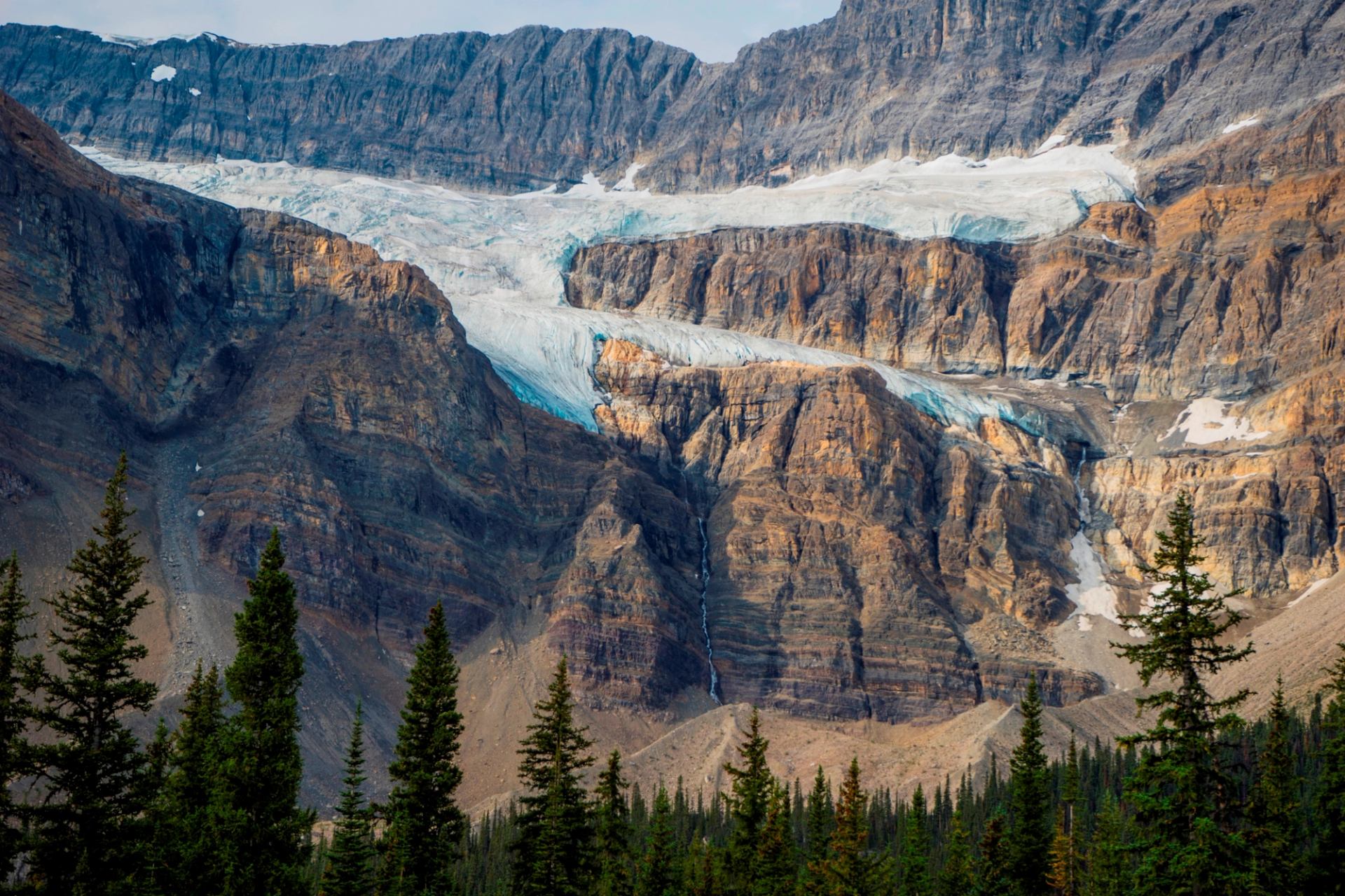 Glacier spans layered mountain cliffs above a dense evergreen forest.