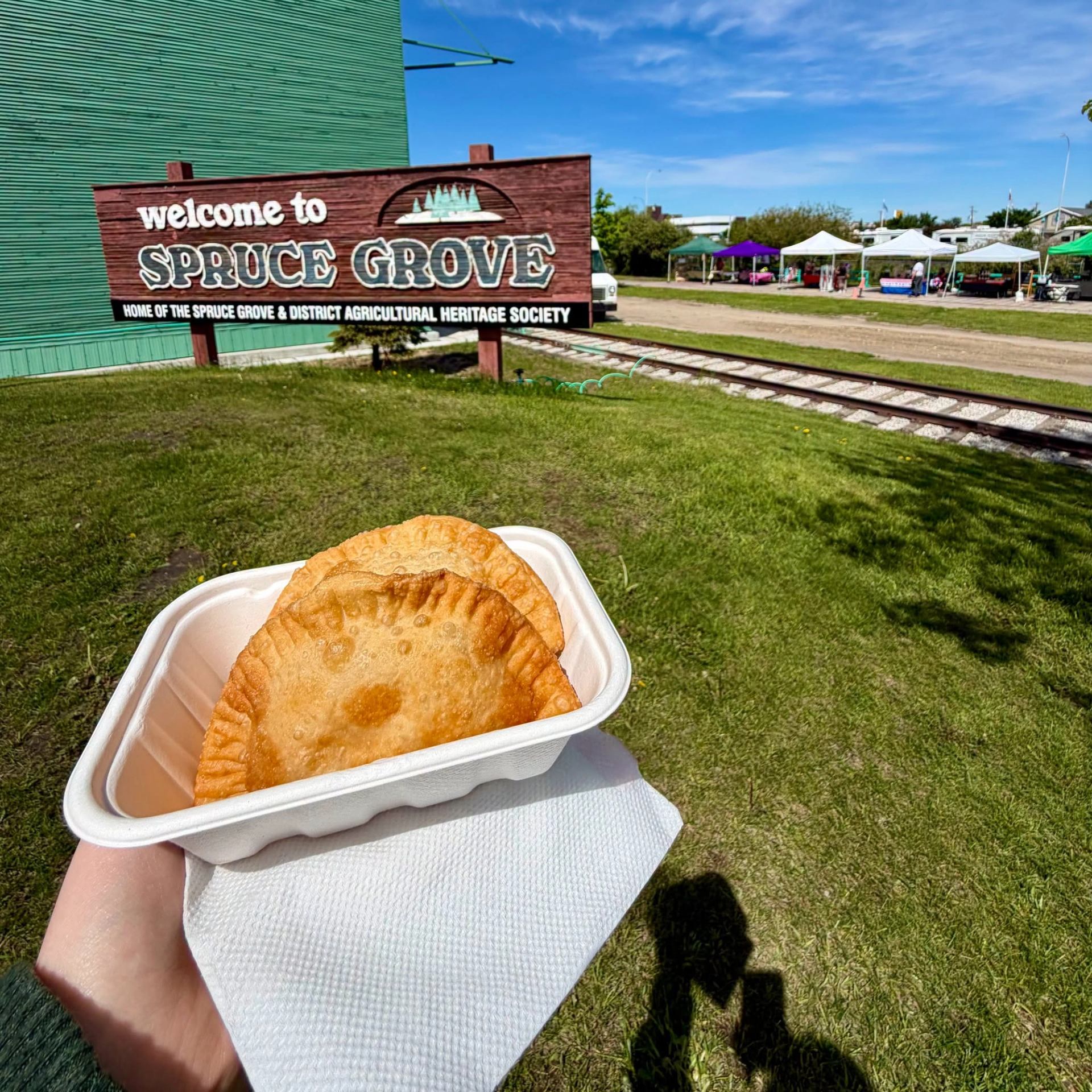 Fresh pastries are served outdoors near market tents and a community heritage site sign.