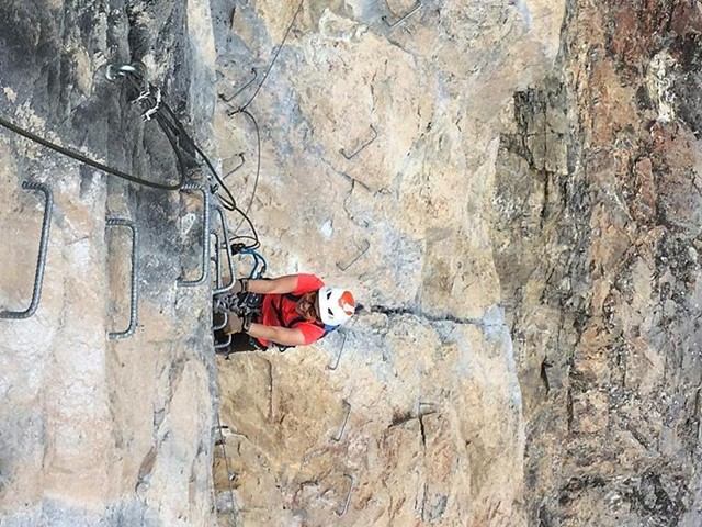 A person in a white and red helmet climbs a metal ladder fixed to a rocky mountainside during a climbing adventure.