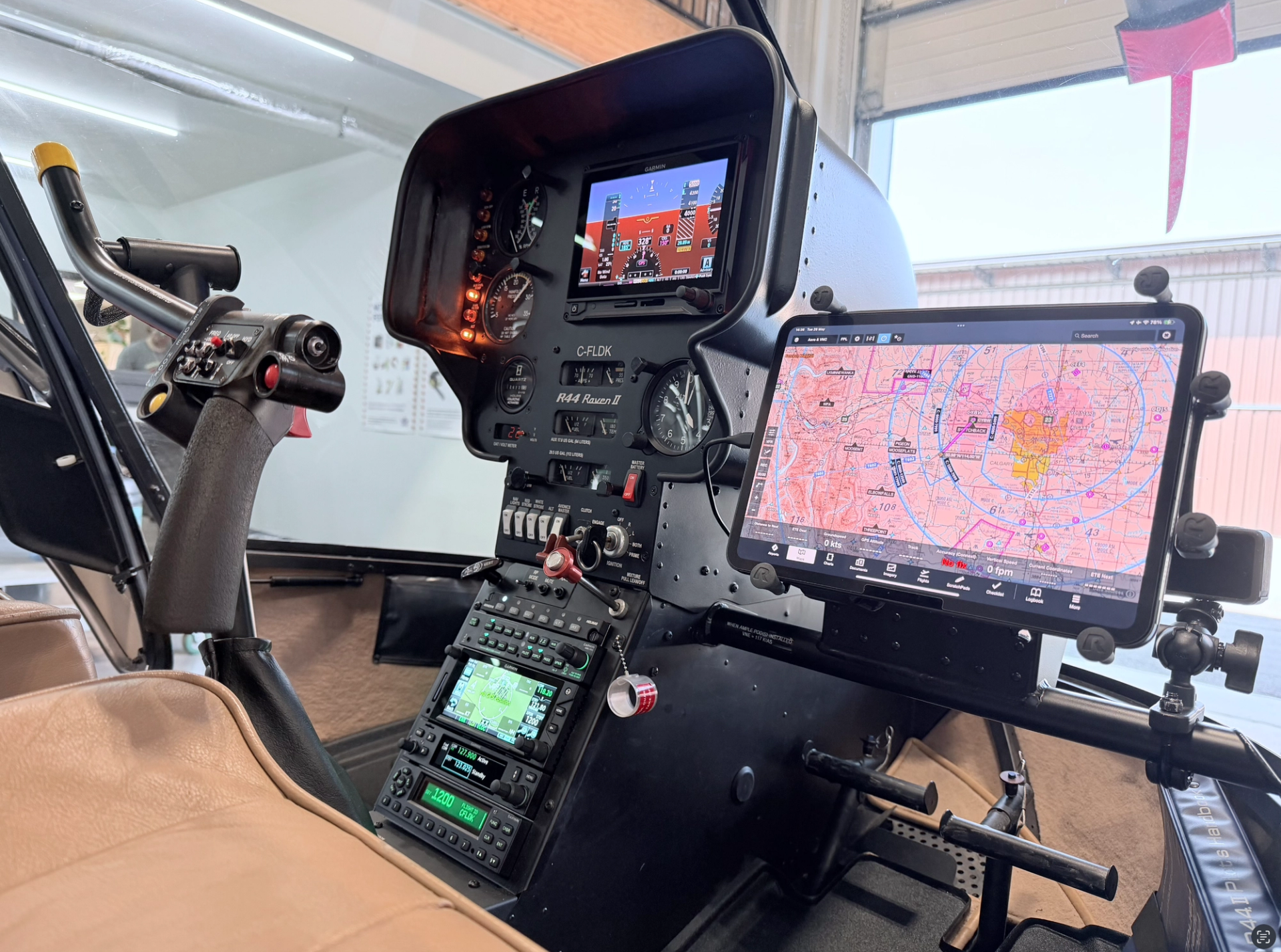 Helicopter cockpit with digital flight instruments and tablet displaying detailed aeronautical navigation chart.