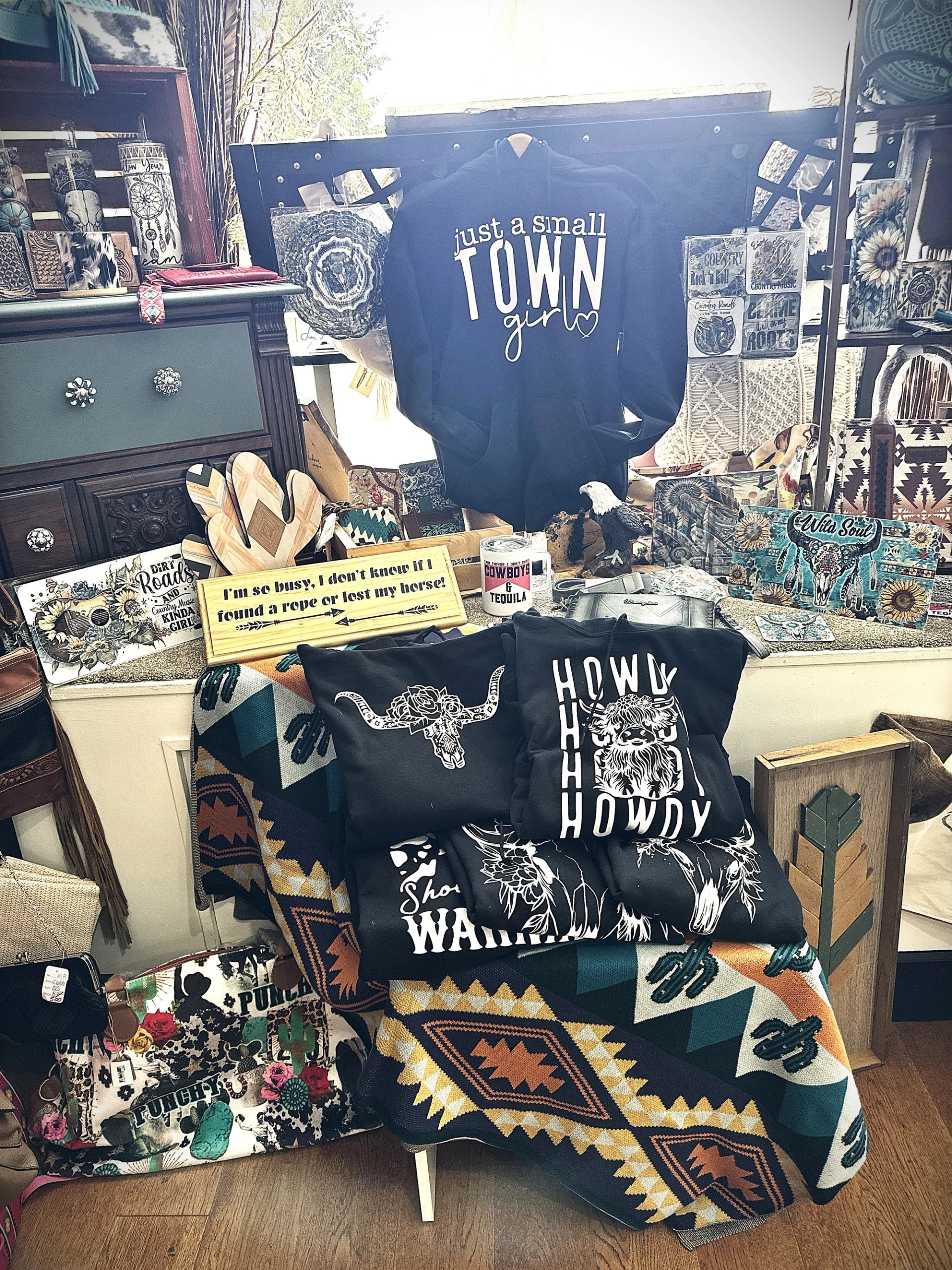 Display of Western‑themed shirts, signs, textiles, and accessories arranged on a table.