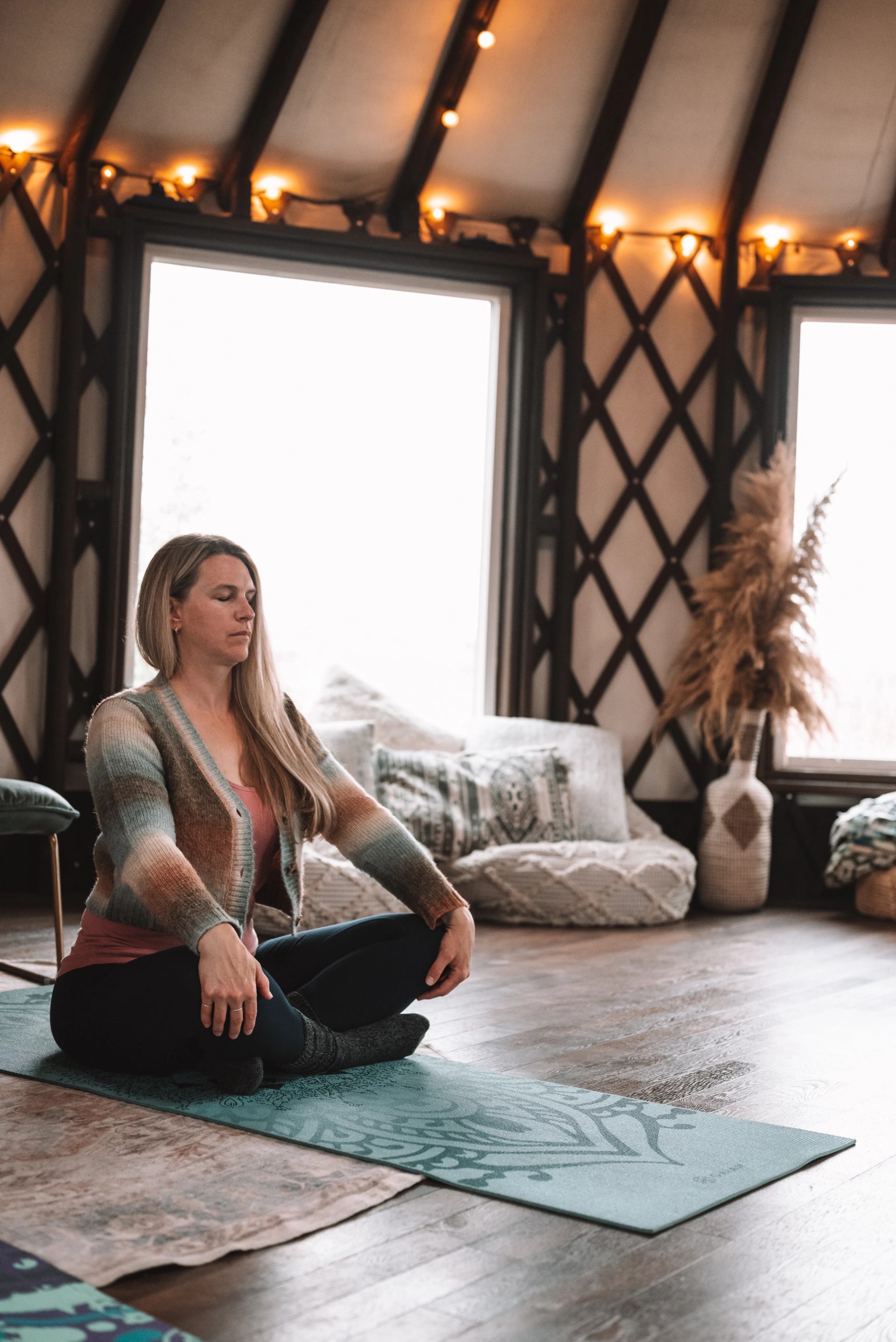 Person sits cross-legged with closed eyes on a yoga mat inside a yurt.