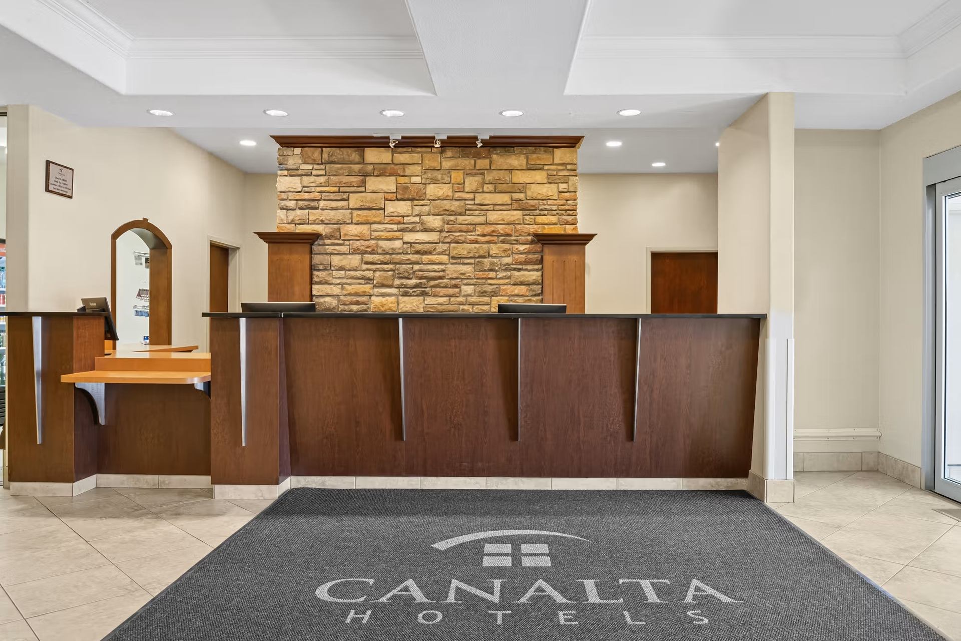 Hotel reception desk with stone accent wall and Canalta Hotels logo mat.