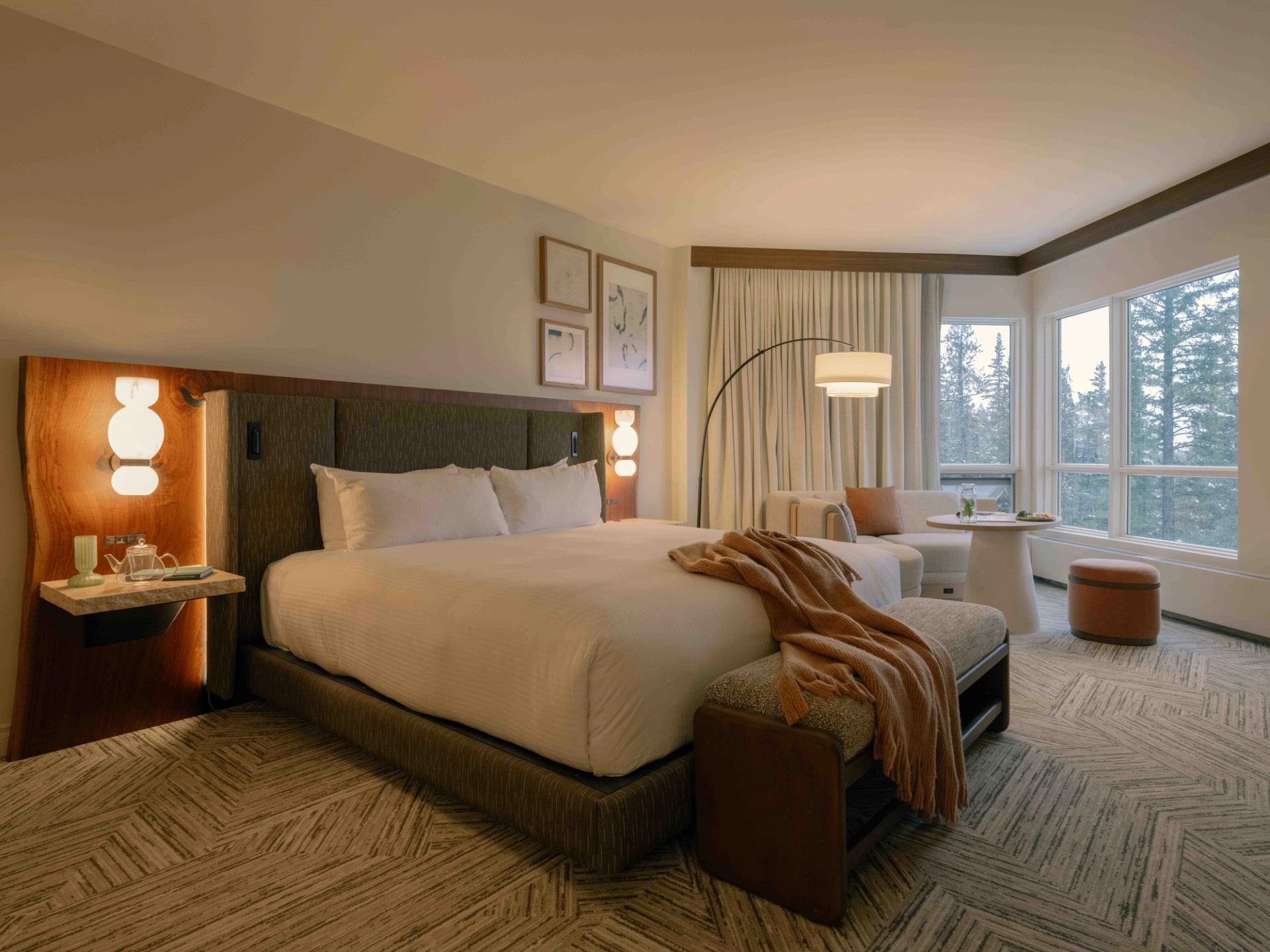 Stylish hotel guest room with a king bed, soft lighting, seating area, and large windows overlooking forest at Rimrock Banff.