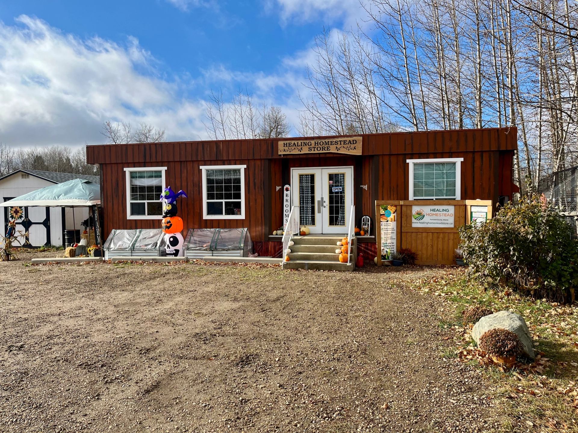 Rustic farmhouse building with seasonal decorations and trees in the background.