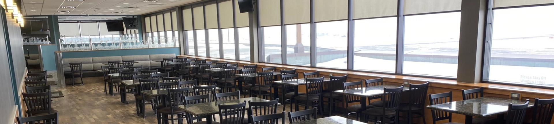Empty airport restaurant with rows of tables, chairs and large windows overlooking runways.