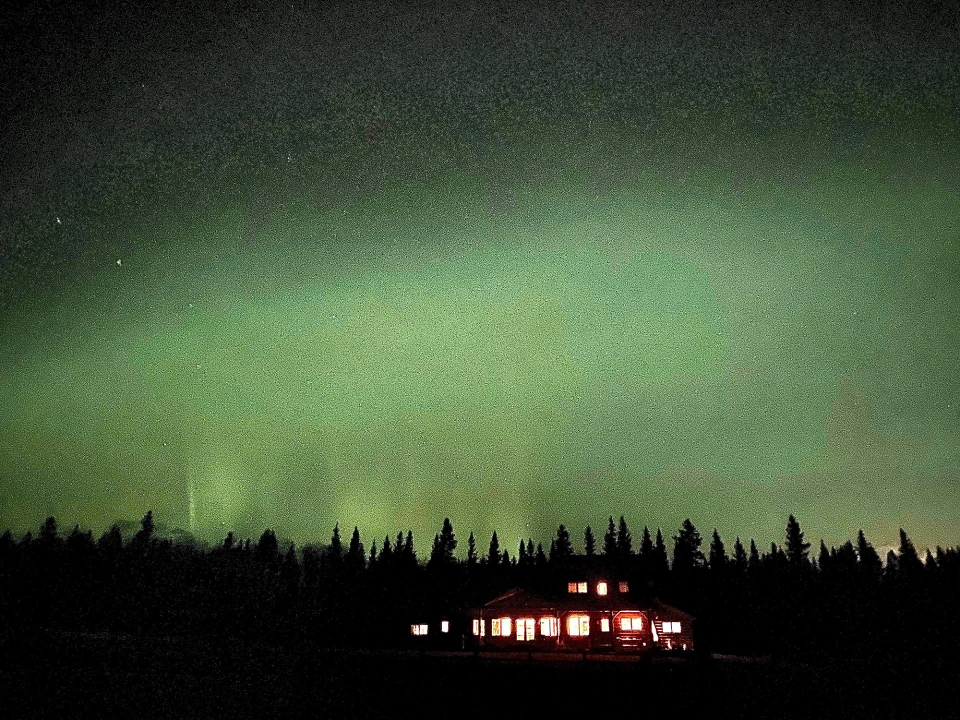 Aurora borealis illuminates the night sky above a dark cabin, creating a serene and magical atmosphere.