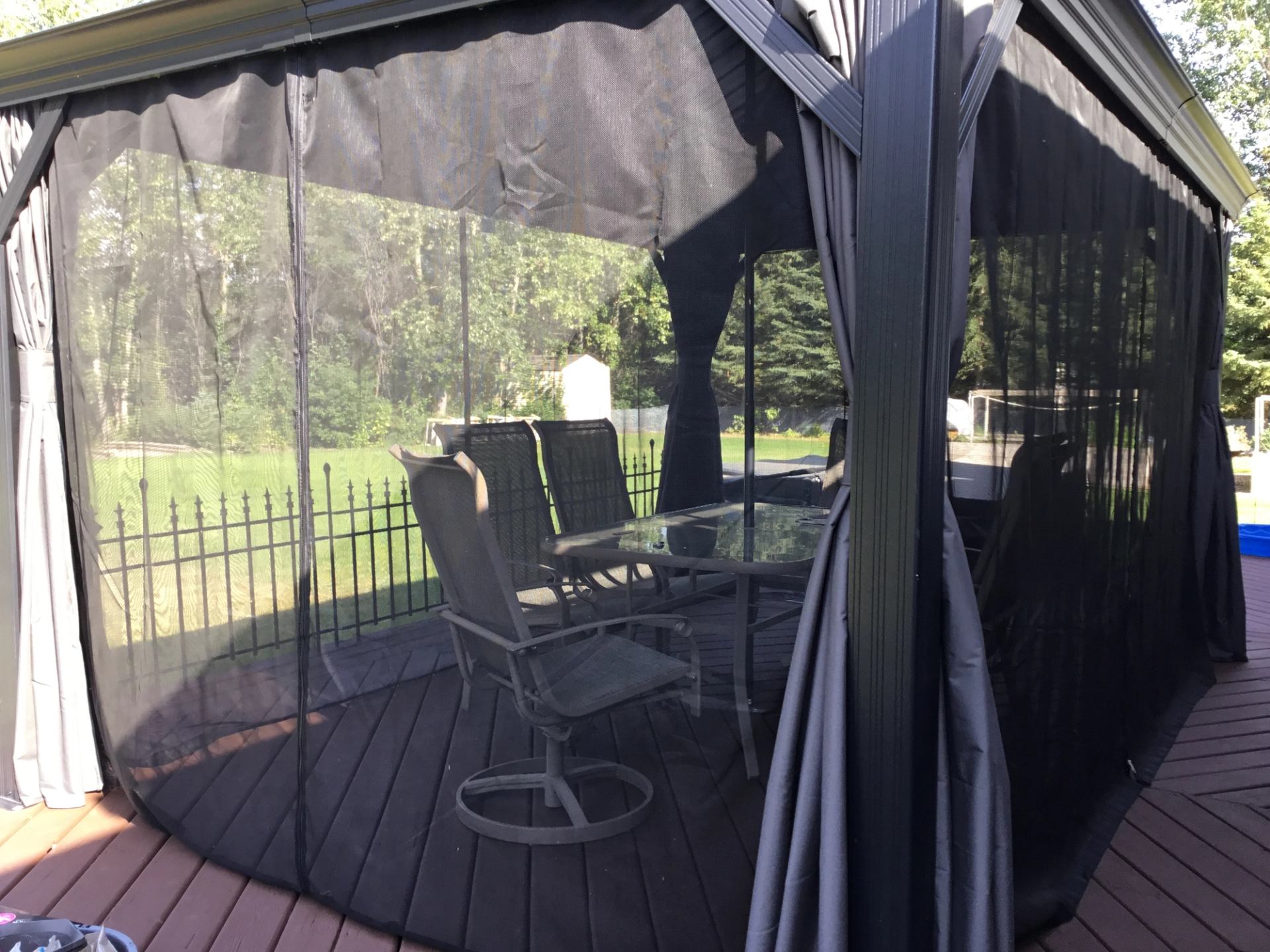 Screened gazebo on wooden deck with patio table, chairs and backyard lawn visible.