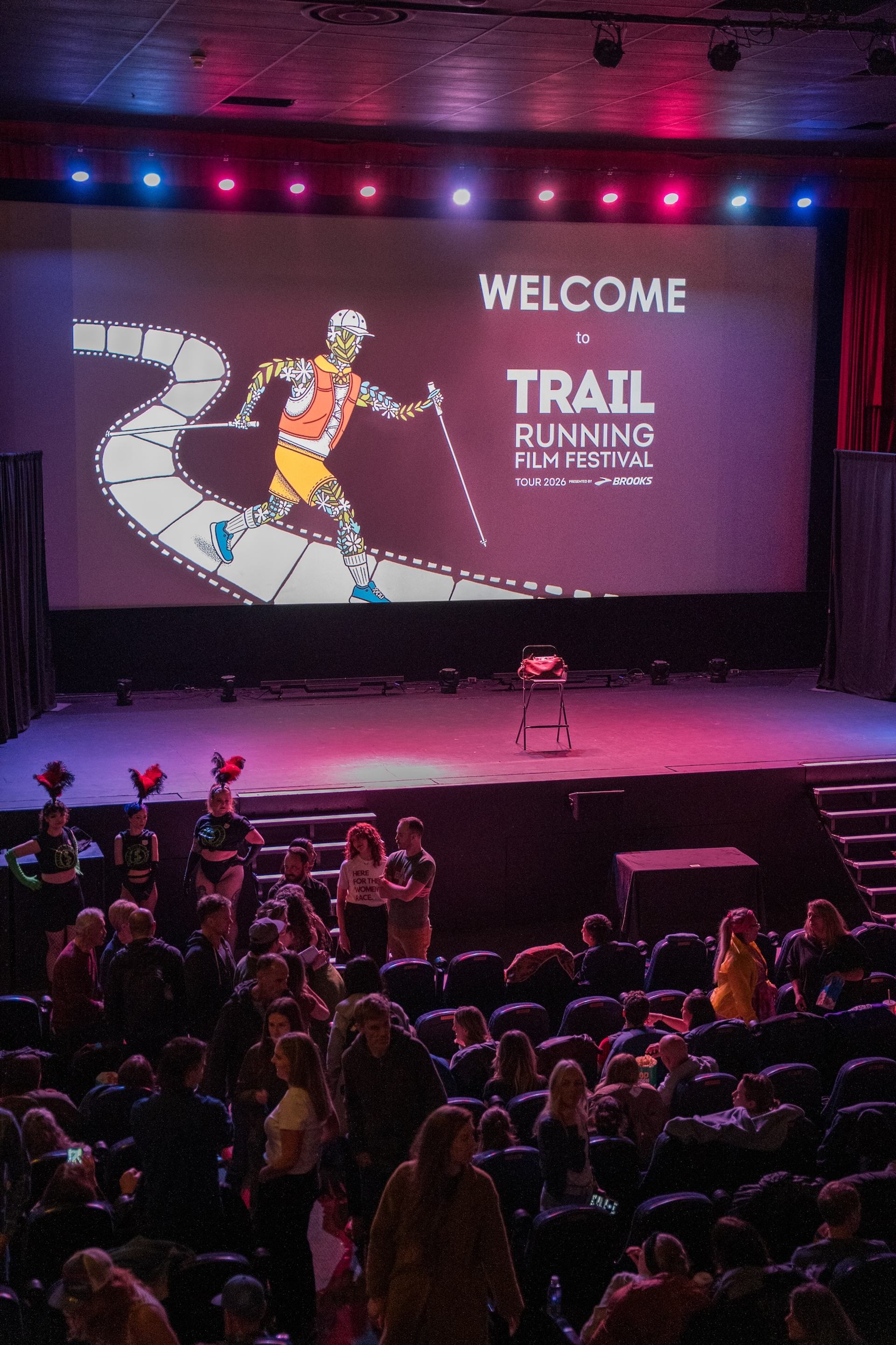 Audience gathers in theatre before Trail Running Film Festival screening with illustrated runner.