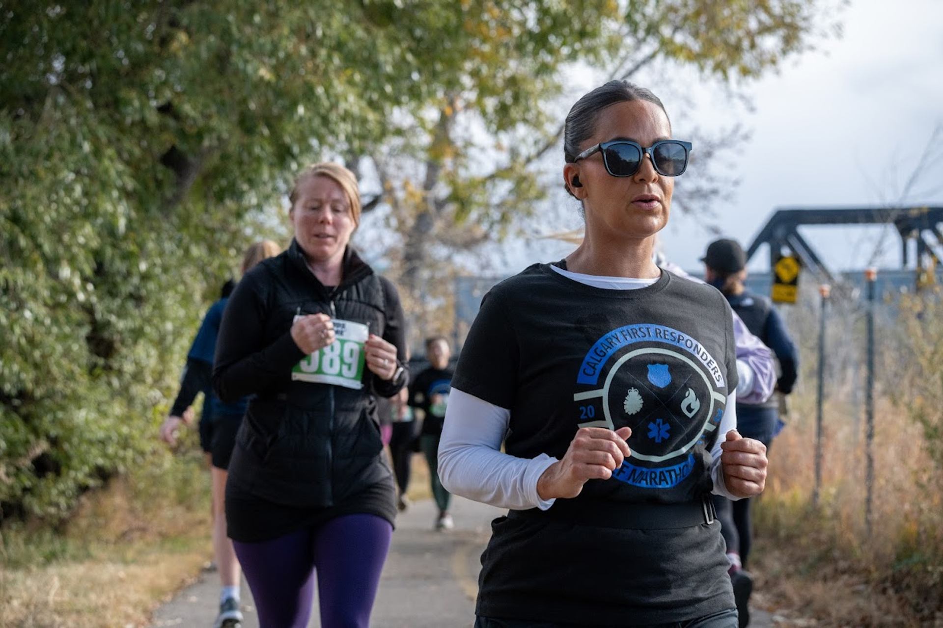 Runners on a paved trail surrounded by trees during a race.