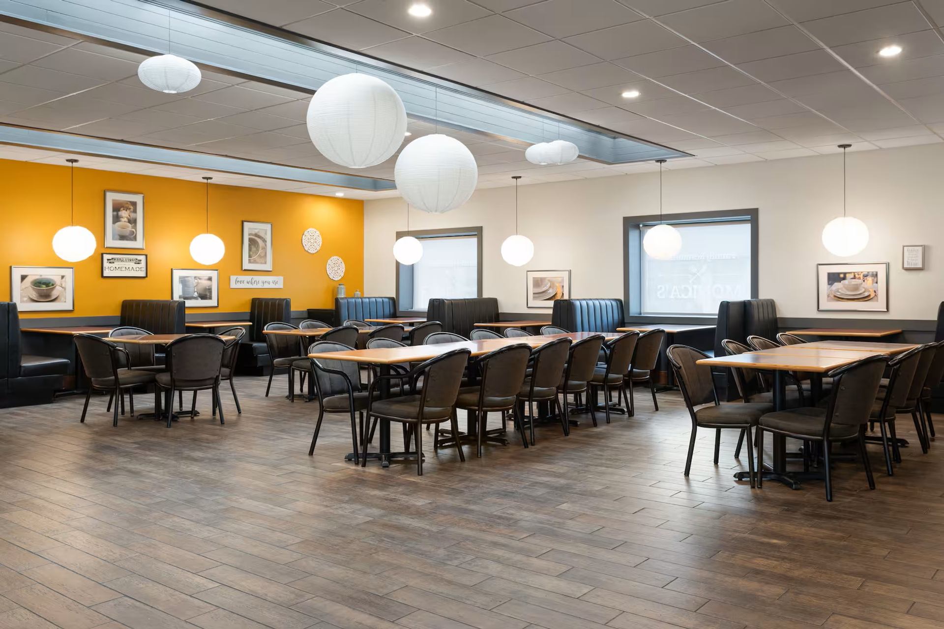 Modern dining area with booth and table seating, orange accent wall, and hanging lights.