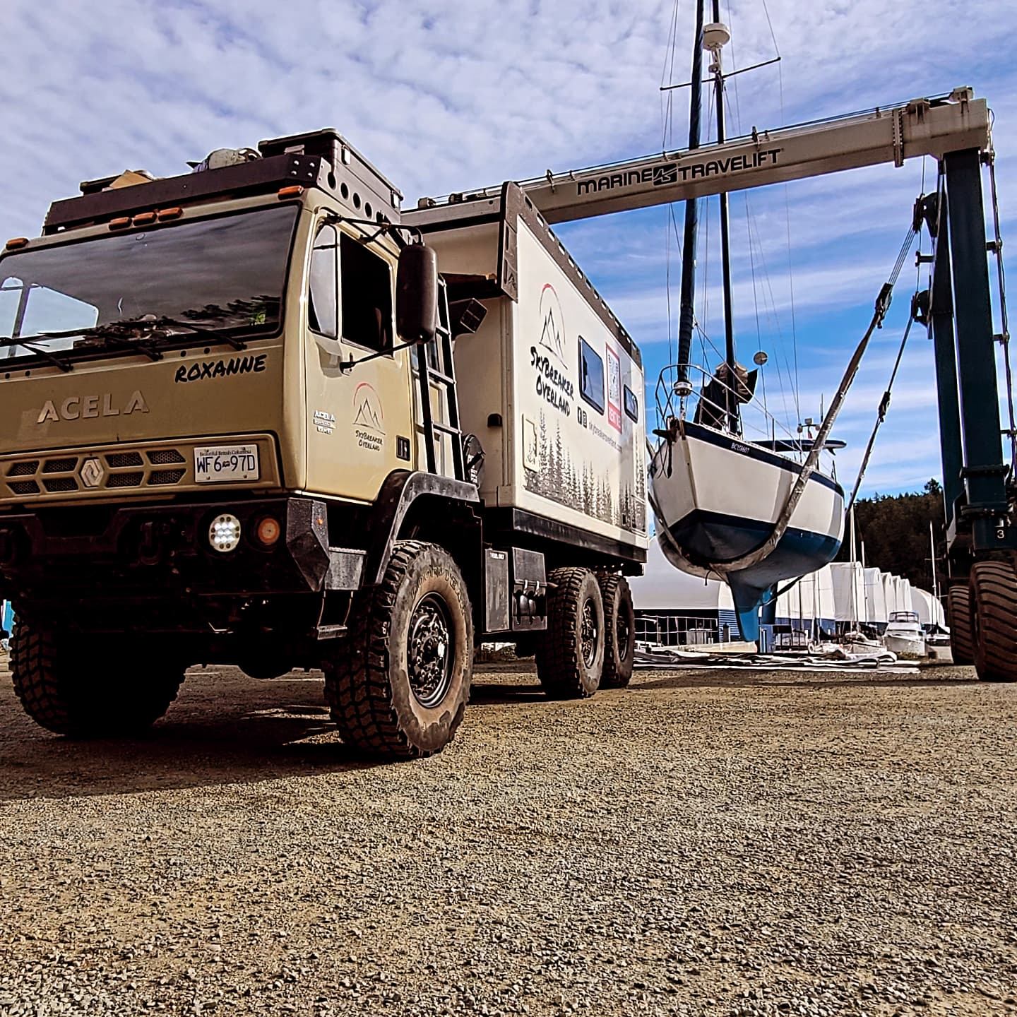 Acela expedition truck at marina with container and boat lift in background.
