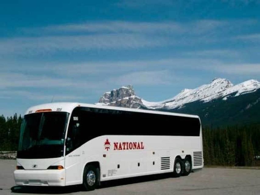 White bus with 'NATIONAL' logo near snow-capped mountains and blue sky.