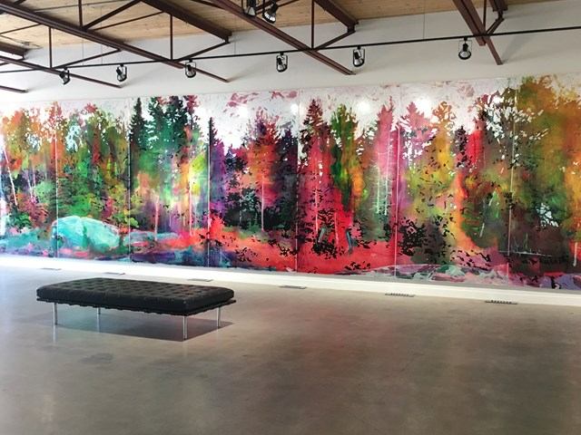 Art gallery interior with a colorful forest mural and a black bench on the floor.