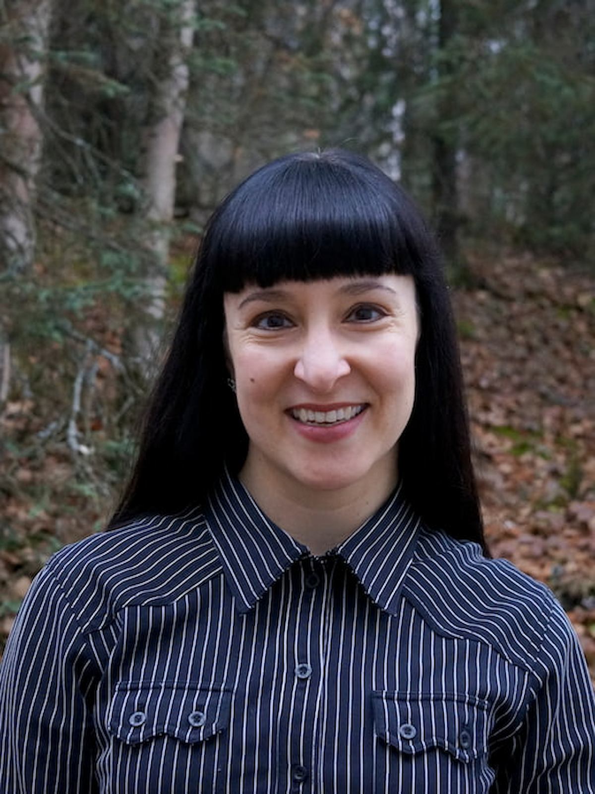 Woman portrait outdoors with trees and hills in the background.
