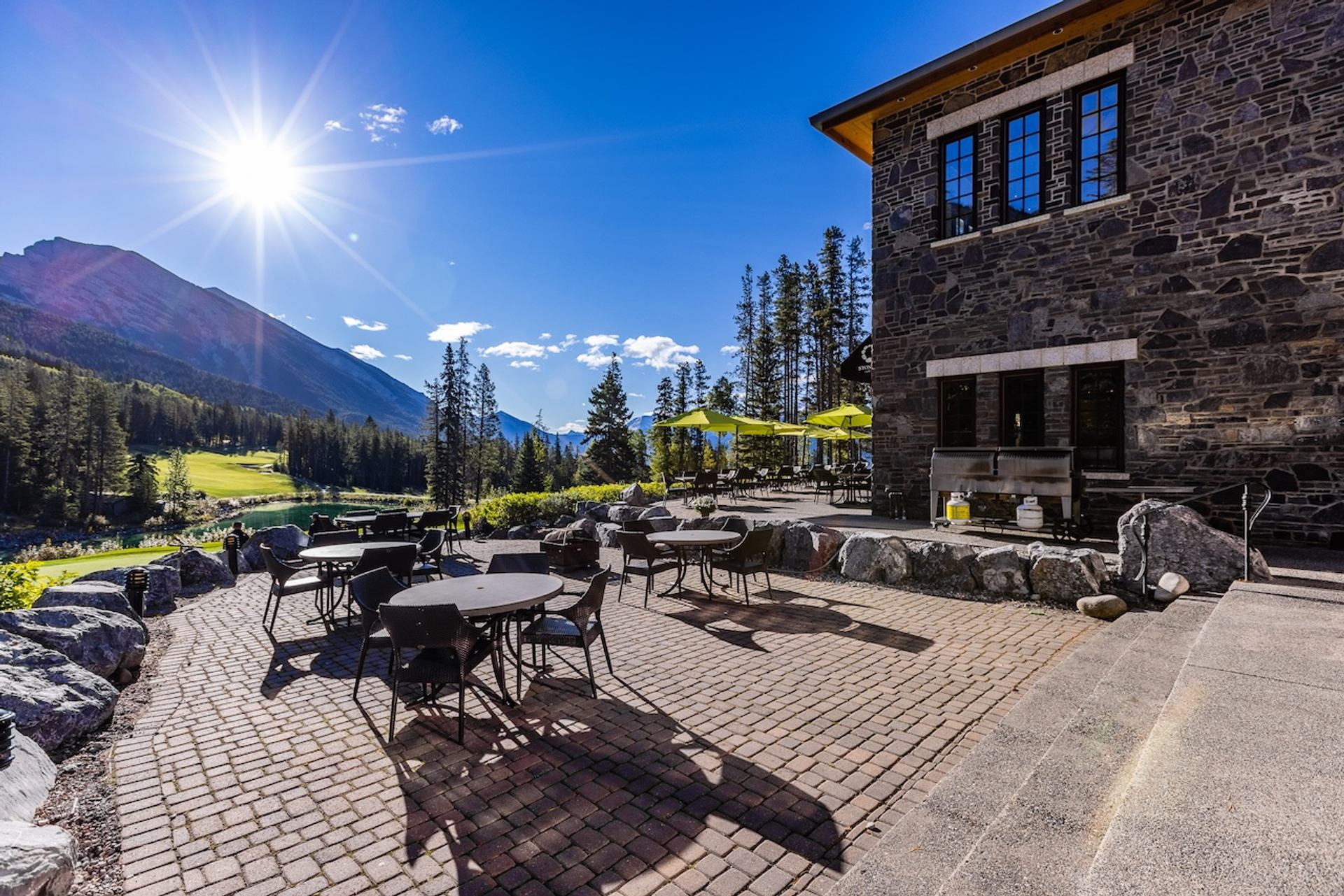 Patio with tables overlooking golf greens and mountains under bright sun