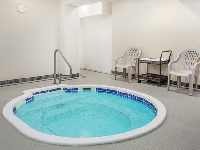 Indoor hot tub with blue tile accents, white walls, and plastic chairs in a simple spa area.