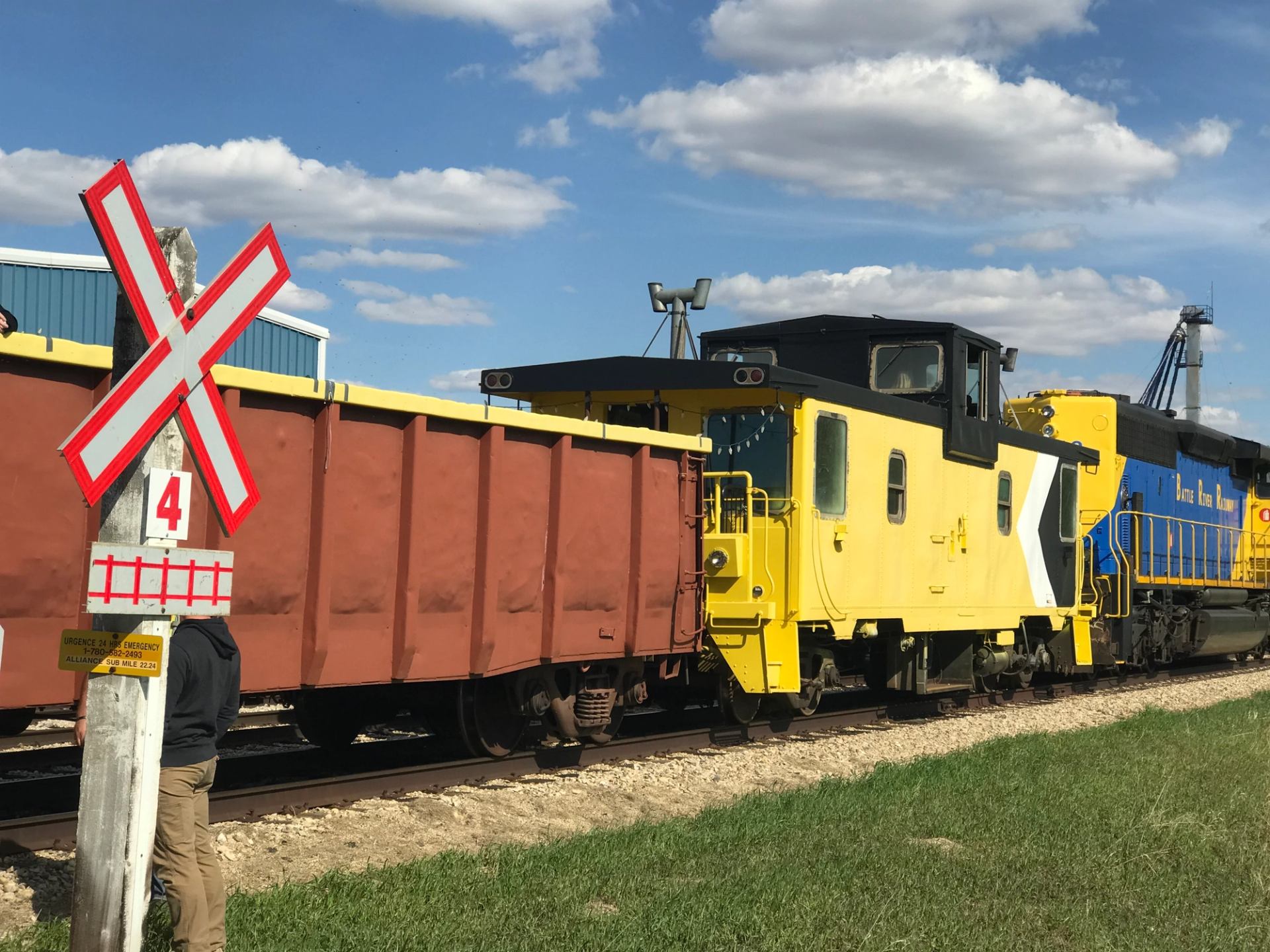 Yellow and brown train cars stopped on tracks near a railway crossing.