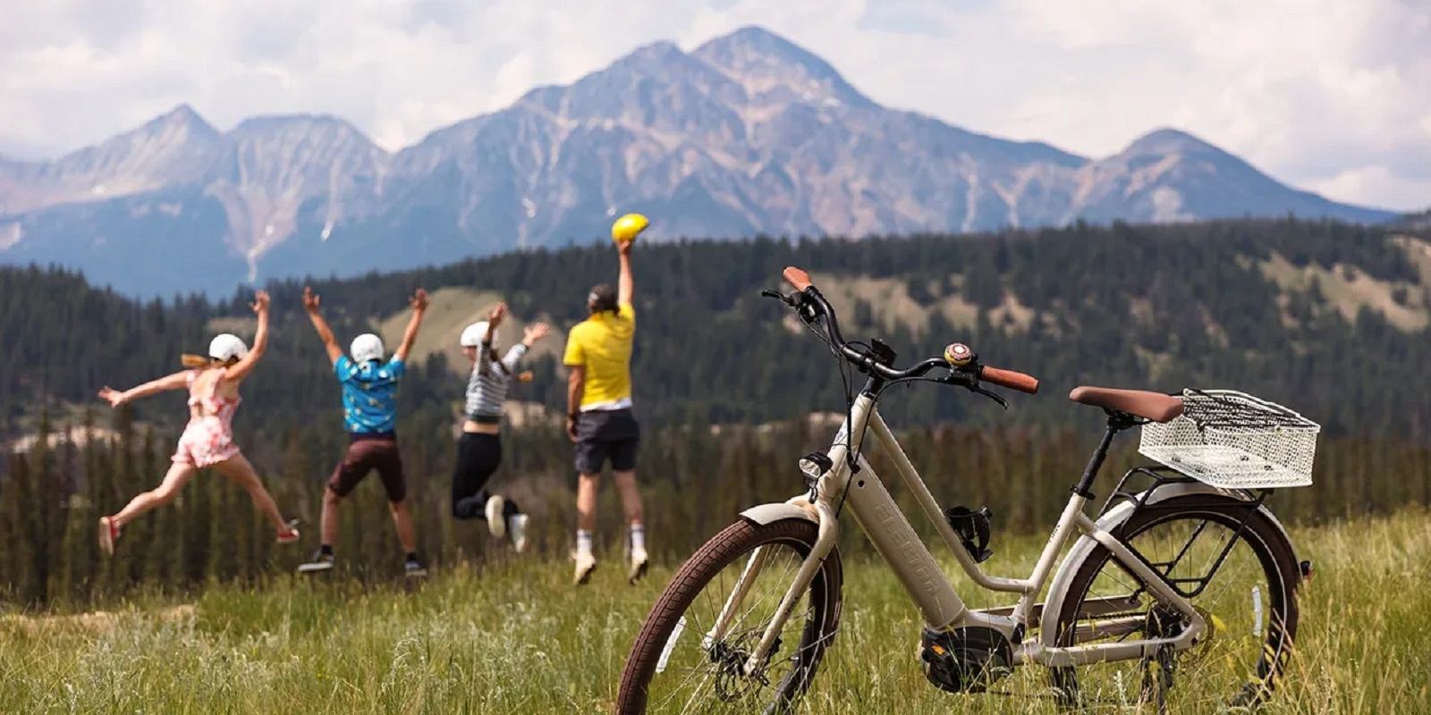 E-bike on grassy field with people playing frisbee and mountains in the background.