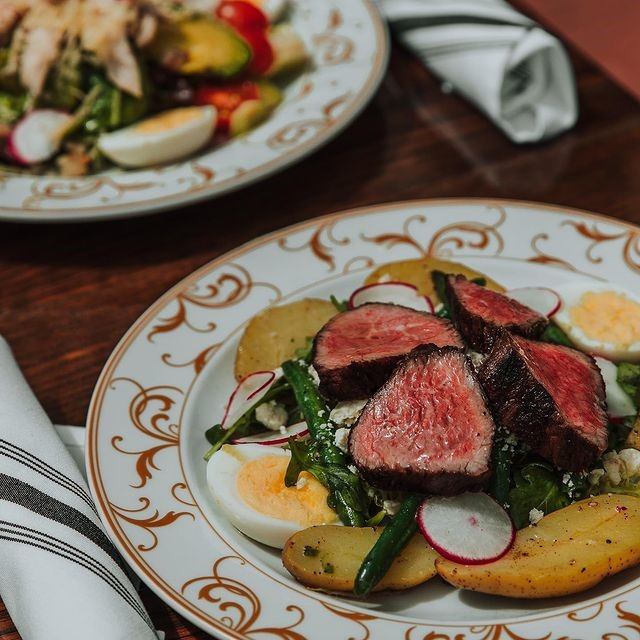 Gourmet plates with steak, veggies, and eggs on ornate dishes at The Guild.