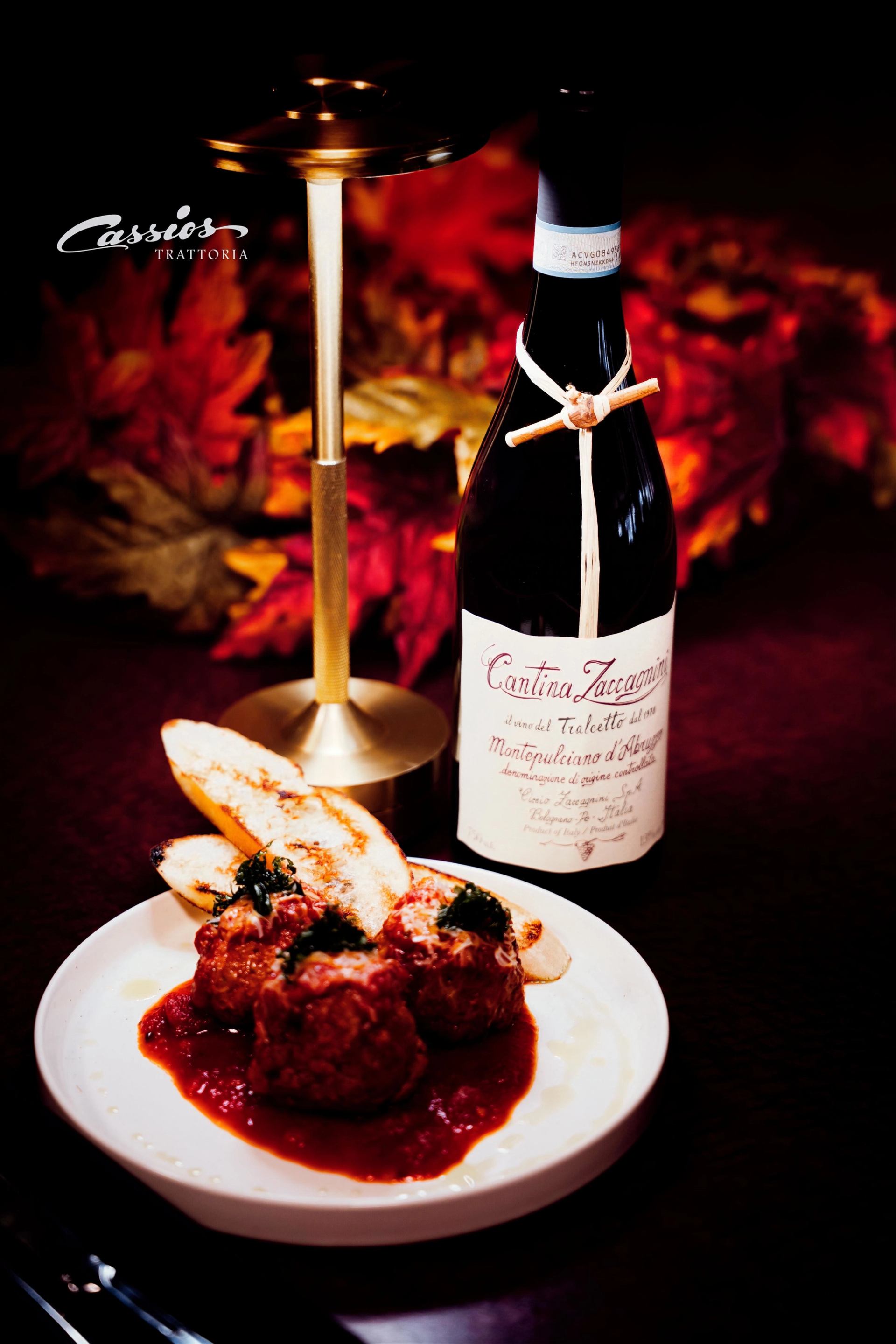 Plate of meatballs in tomato sauce with toasted bread beside red wine bottle.