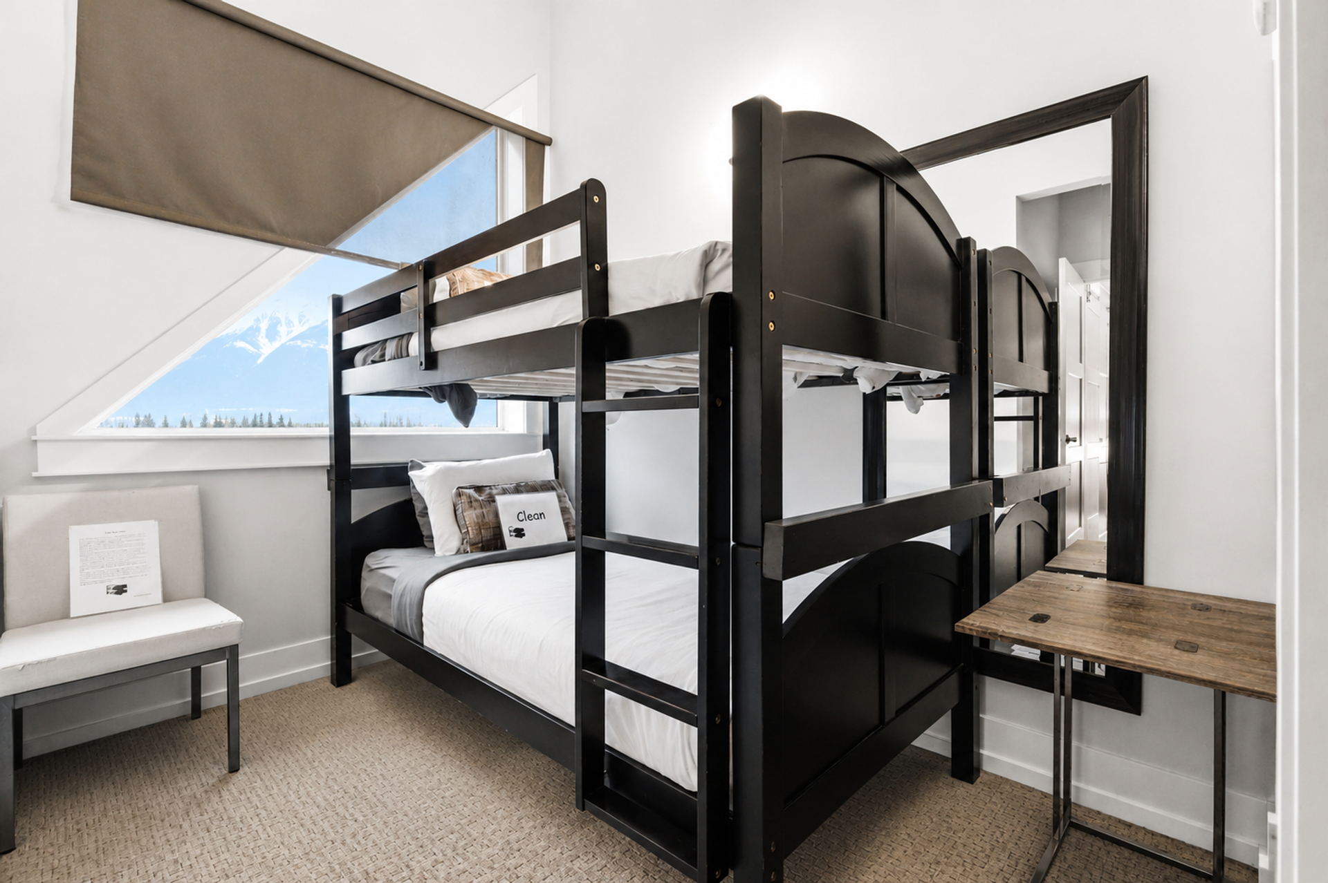 Bedroom with two black bunk beds, a triangular window, chair and wooden table.