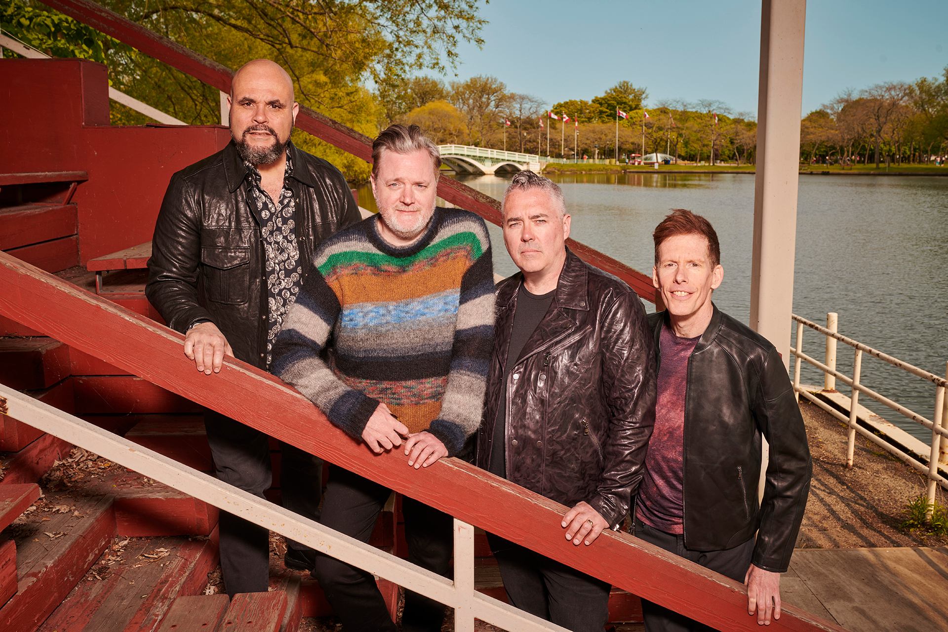 Four people stand on red wooden stairs beside a calm river and trees.