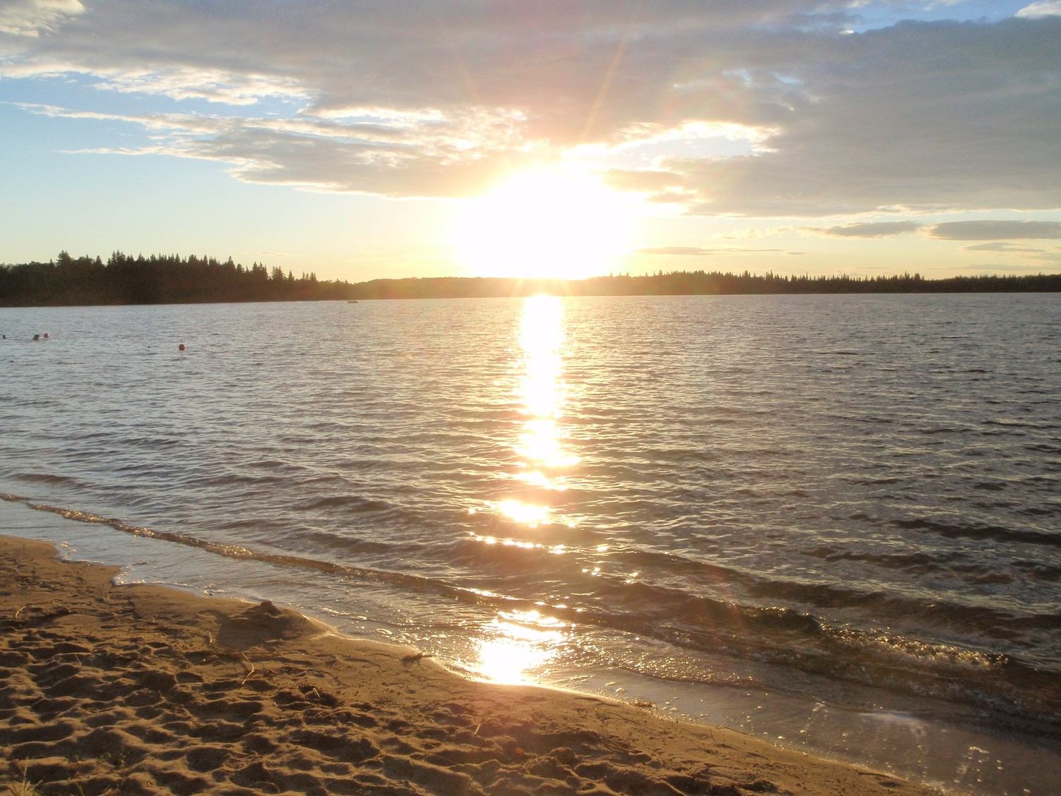Golden sun setting over sandy shoreline and calm lake water