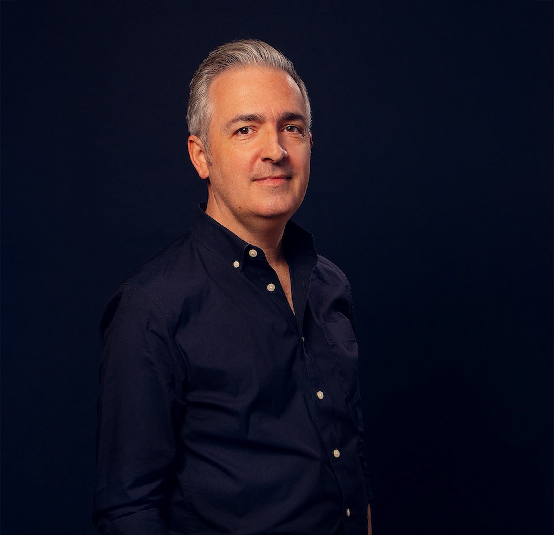 Matt Madden standing in dark shirt against a black background.