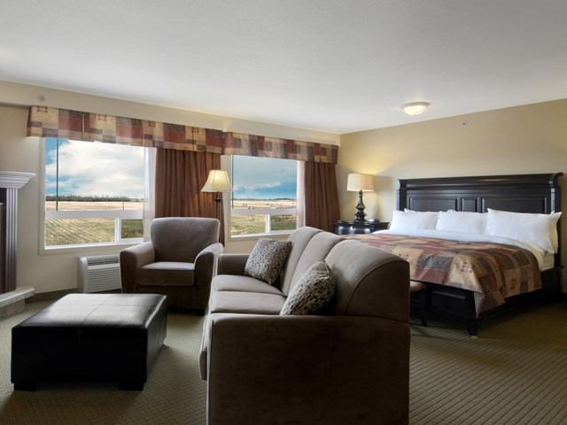 Spacious hotel room with bed, sofa, armchairs, and large windows.
