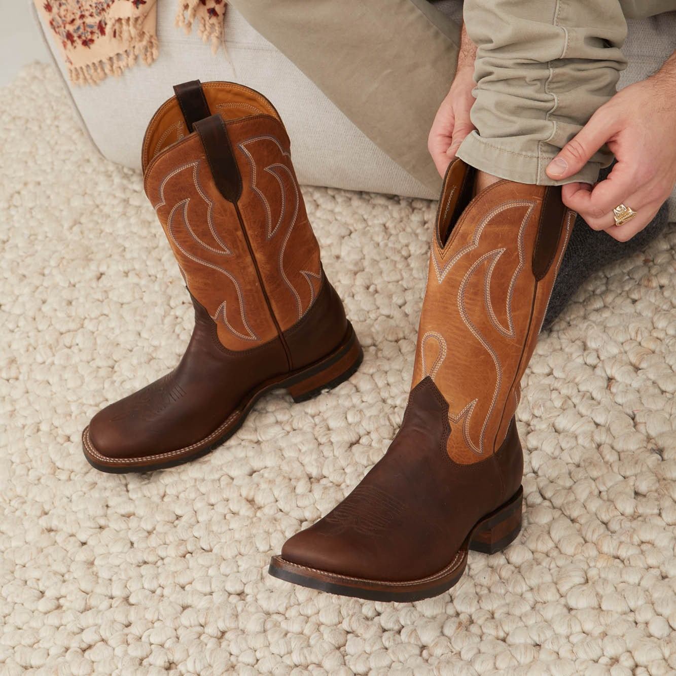 Pair of brown cowboy boots with stitched patterns and hand holding the cuff.