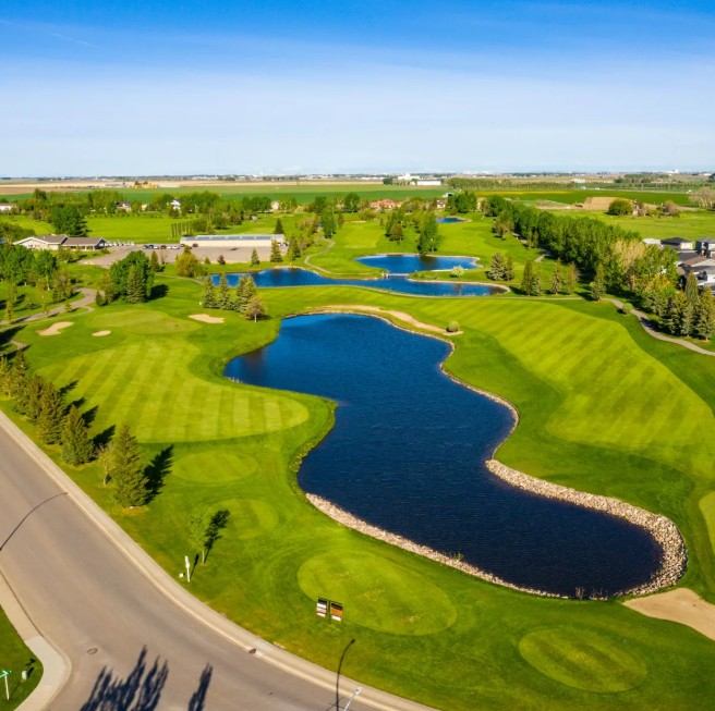 Aerial view of lush green fairways with winding ponds under a clear blue sky